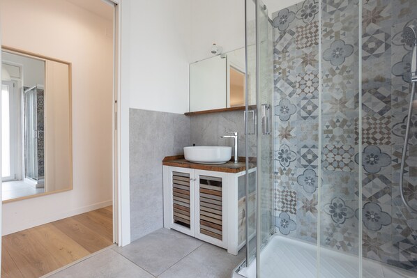A modern bathroom with a glass shower enclosure, a wooden vanity, and a large mirror.