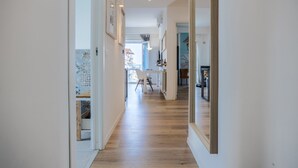 Un pasillo con piso de madera, un comedor con mesa y sillas, y un espejo grande en la pared derecha.