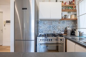 Een keuken met een roestvrijstalen koelkast, een gasfornuis en een betegelde spatwand.