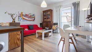 Un moderno salón con un sofá rojo, un aparador de madera, una mesa de comedor y un gran ventanal con cortinas.