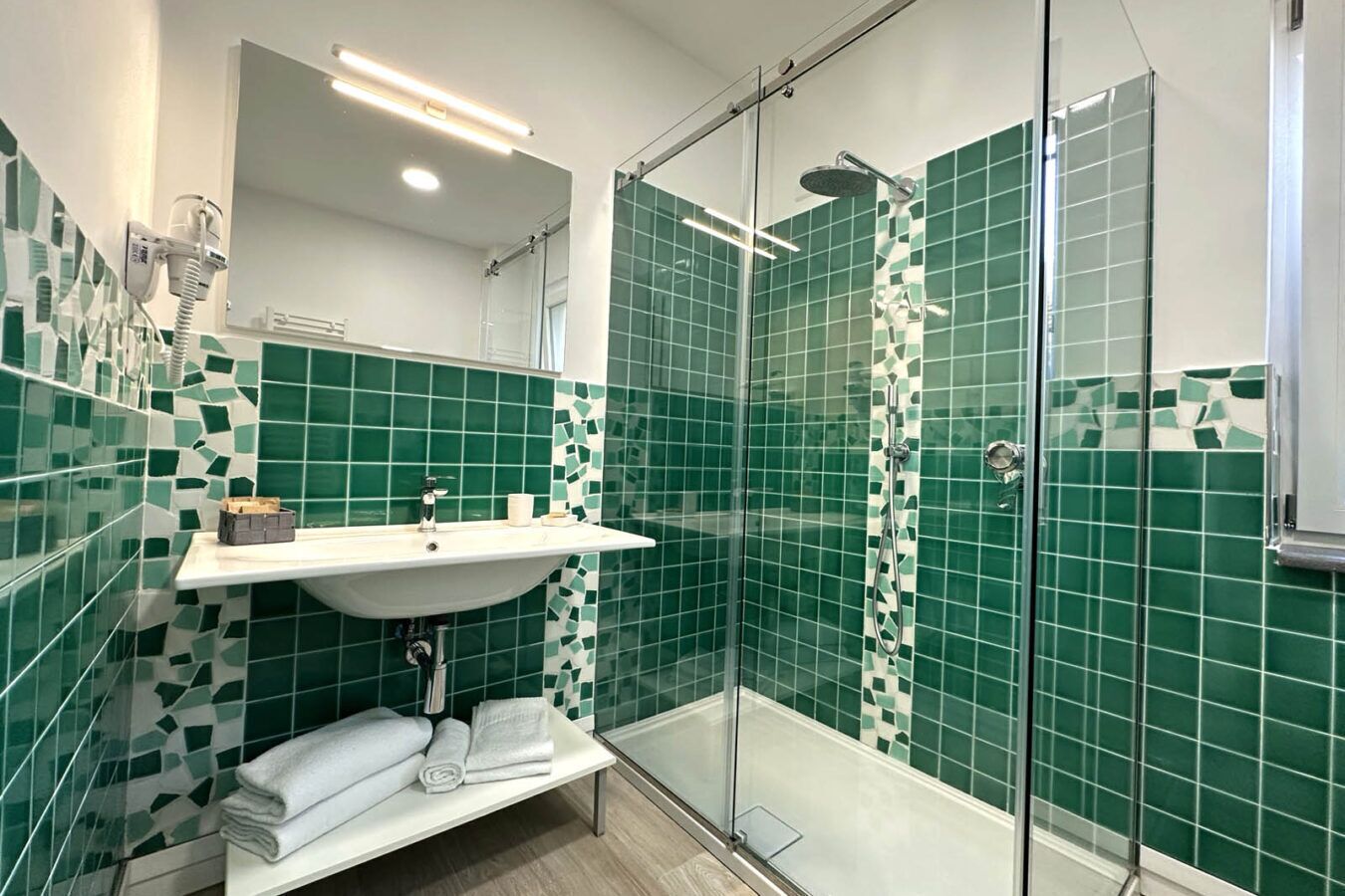 A modern bathroom with a glass-enclosed shower, a white sink, and green mosaic tiles.