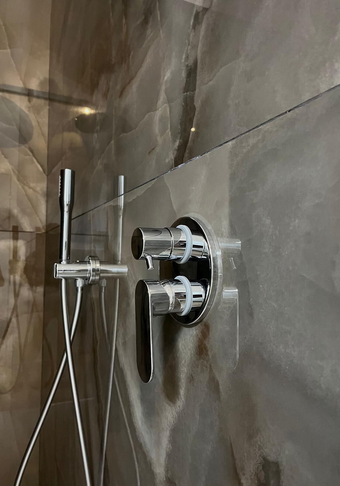 A shower with chrome fixtures against a marble wall.