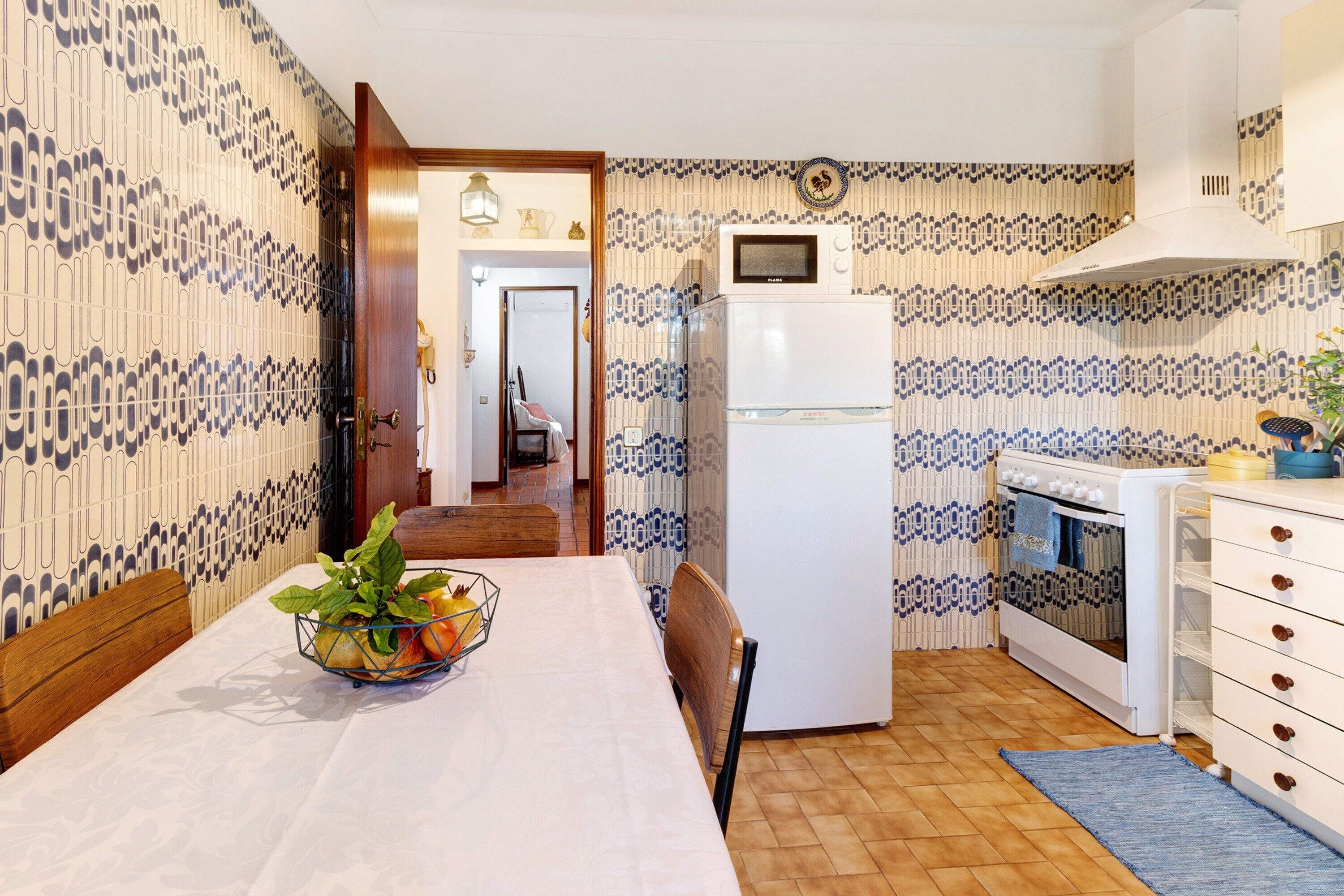 A kitchen with patterned wallpaper, a white refrigerator, an oven, and a dining table with chairs.