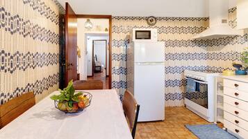 A kitchen with patterned wallpaper, a white refrigerator, an oven, and a dining table with chairs.
