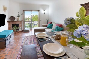 Ein Essbereich mit einem Tisch für vier Personen, einem Kamin, einer Couch mit Kissen und Blick durch eine Glastür.