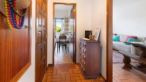 A hallway with a wooden door, a dining area with a table and chairs, a wooden dresser, and a sofa with cushions.