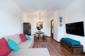 Ein Wohnzimmer mit einer Couch, einem Fernseher, einem Tisch mit einer Vase und einem gemusterten Teppich.