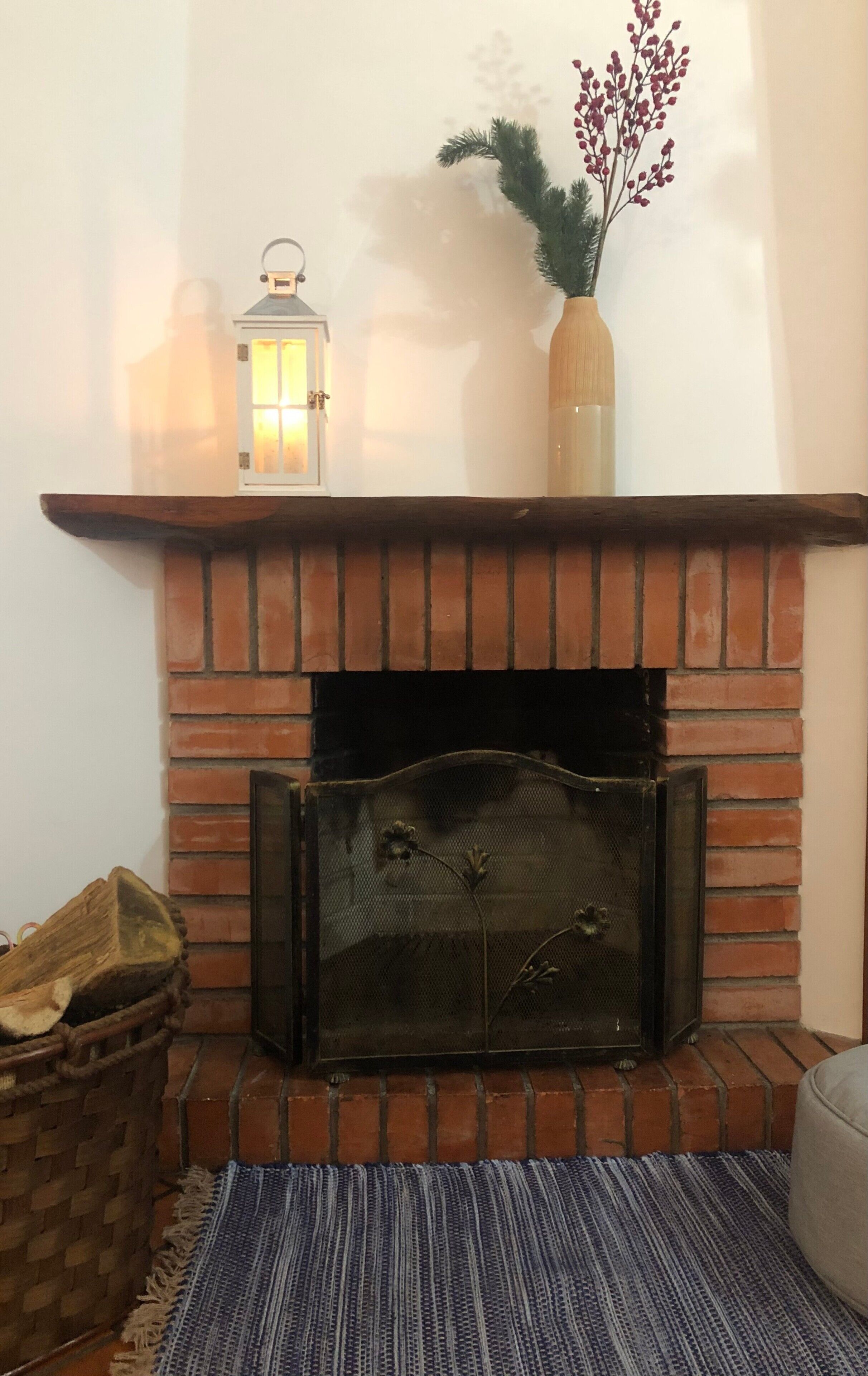 A fireplace with a brick surround, a decorative lantern, and a vase with red berries.