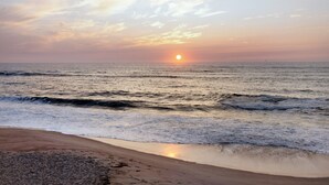 A beach with waves, a sunset, and a clear sky.
