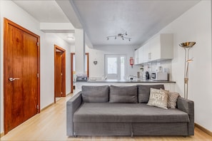 A modern living room with a grey sofa, wooden doors, and a kitchen in the background.