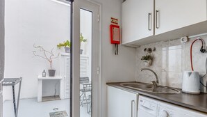 A compact kitchen with a washing machine, a sink, and a small dining area visible through a sliding door.