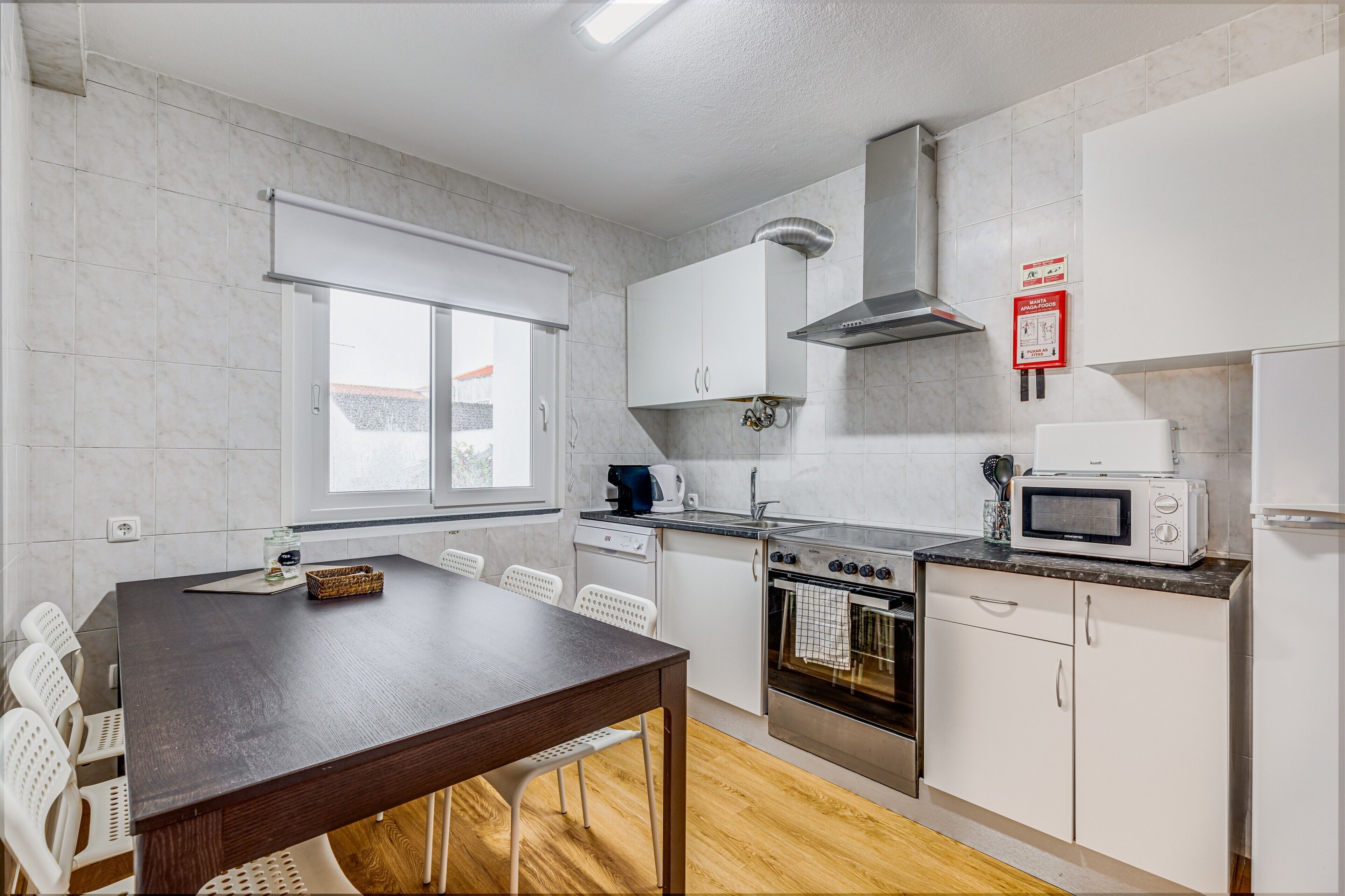 Una cucina moderna con mobili bianchi, forno integrato, microonde e una finestra.