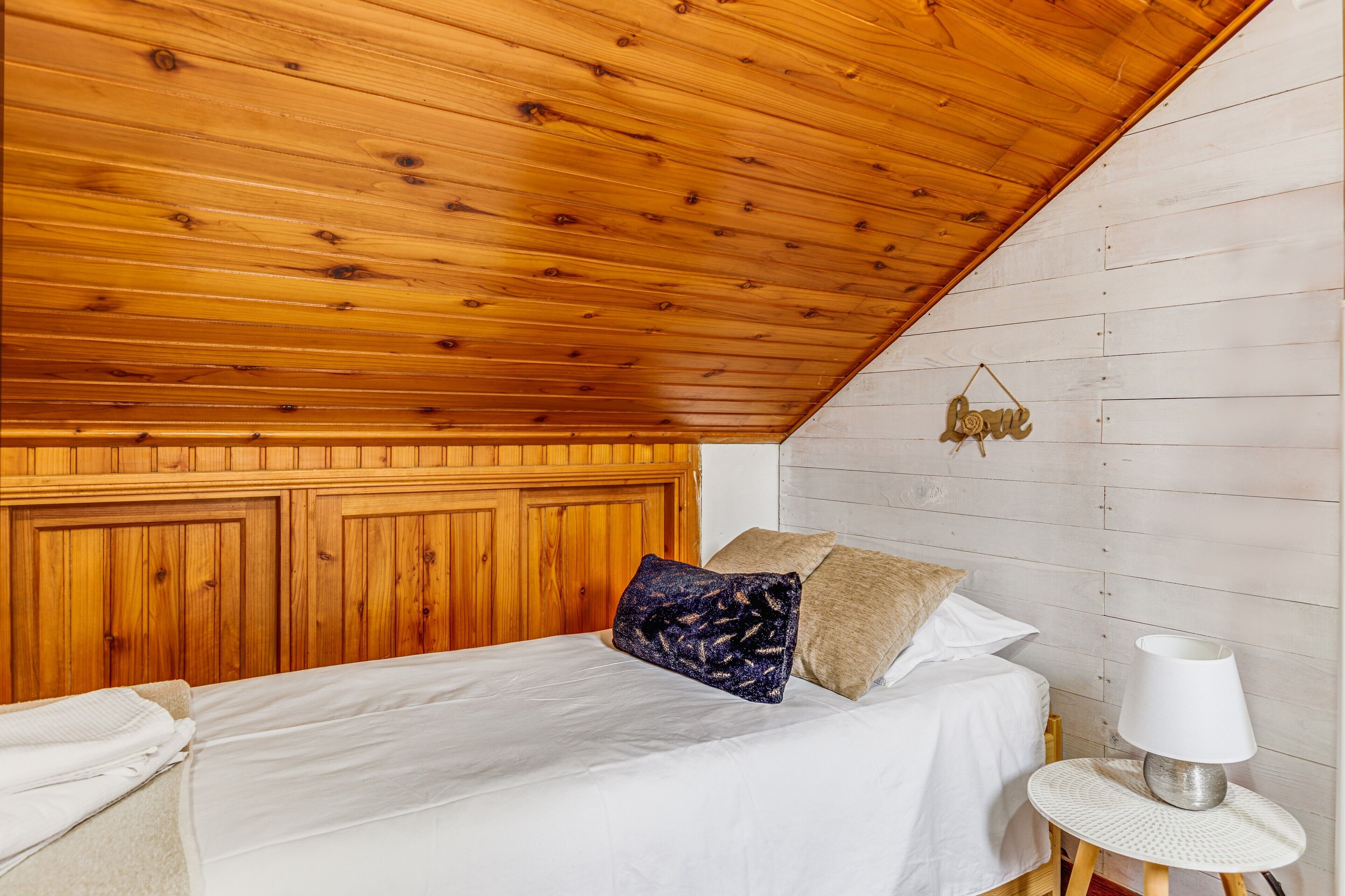Ein Schlafzimmer mit Holzboden, einem Bett mit weißer Bettwäsche, einem blau gemusterten Kopfkissen und einer Nachttischlampe.