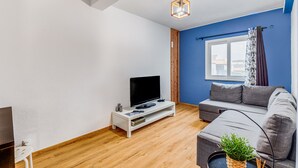 A modern living room with a flat-screen TV on a white stand, a grey sofa, a wooden floor, and a window with curtains. - Apartment 'Casa Da Travessa Com 3 Quartos' with Wi-Fi & AC (Horta)