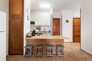 Une cuisine avec un comptoir-bar en bois, des tabourets, des armoires blanches et un dosseret carrelé.