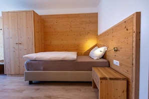 Een kleine kamer met een enkel bed, houten wanden en een bankje.