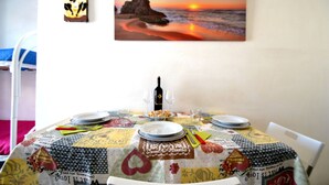 Mesa de comedor dispuesta con platos, vasos y una botella, con una pintura de atardecer en la pared.