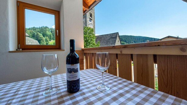 A checkered table with a wine bottle and two glasses on a balcony overlooking a forested landscape. - Holiday Apartment "Gass B" with Mountain View, Private Terrace and Wi-Fi (Laion)