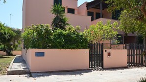 Un immeuble résidentiel doté d’une entrée sécurisée par un portail, d’une allée pavée et d’un petit jardin agrémenté d’arbres et d’arbustes.