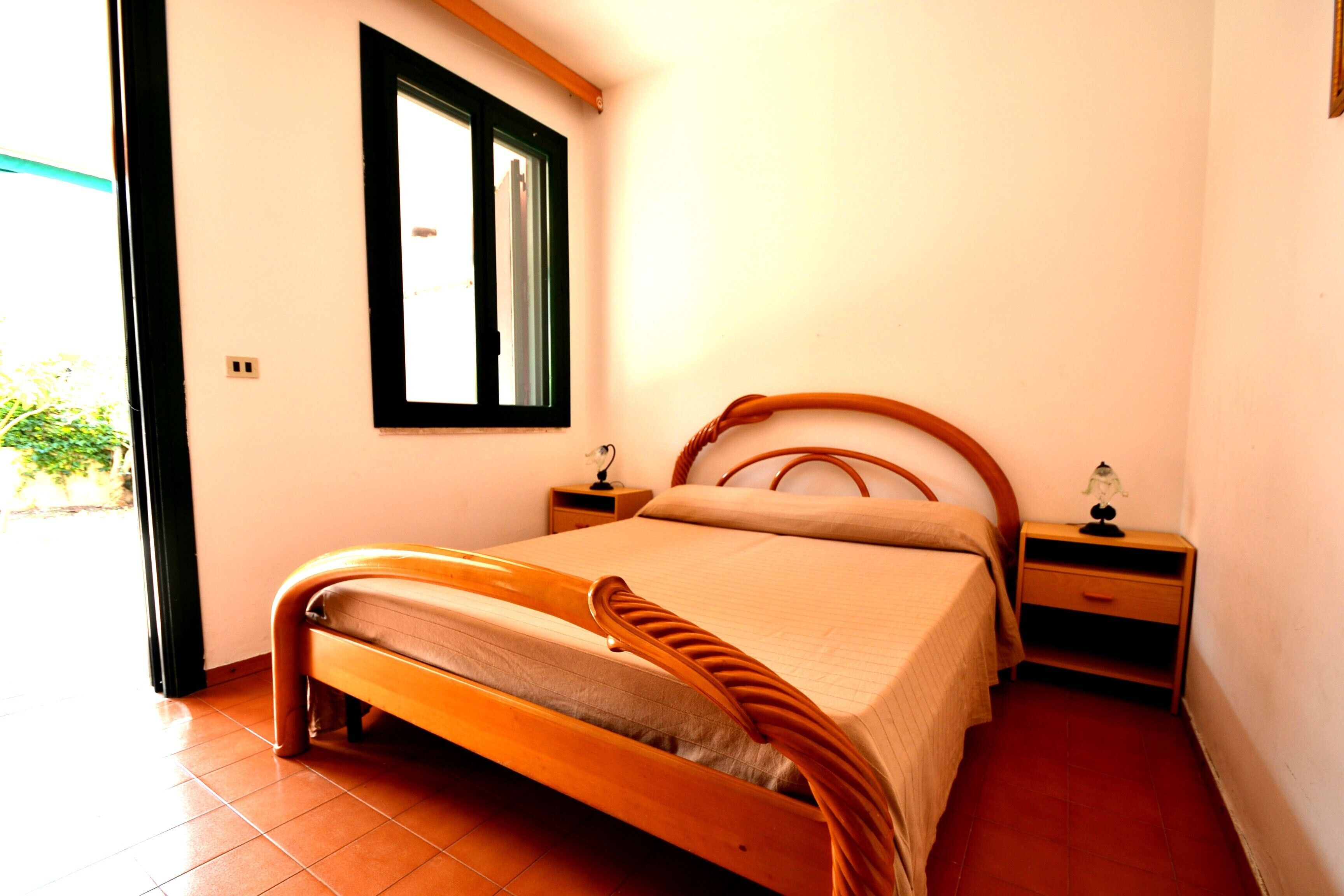 A bedroom with a wooden bed, a nightstand, a bedside table, a window, and a door.