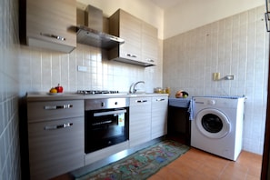 A kitchen with a built-in oven, a washing machine, and a tiled backsplash.