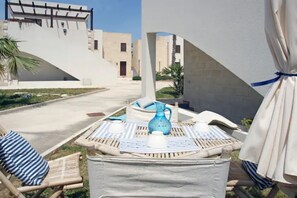 A poolside area with lounge chairs, a table with a pitcher, and a view of the hotel buildings. - La Fuitina in Favignana Holiday House Lido Burrore (Favignana)
