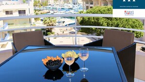 A balcony with a table set for two, featuring a bowl of fruit and two glasses of wine, overlooking a marina with boats and buildings. - Port-fréjus, LE Consul, Appartement 2 Pièces Climatisé, Terrasse & Parking (Fréjus)