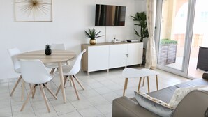 A modern living room with a dining area, white furniture, a flat-screen TV, and a sliding glass door to the outside. - Port-fréjus, LE Consul, Appartement 2 Pièces Climatisé, Terrasse & Parking (Fréjus)