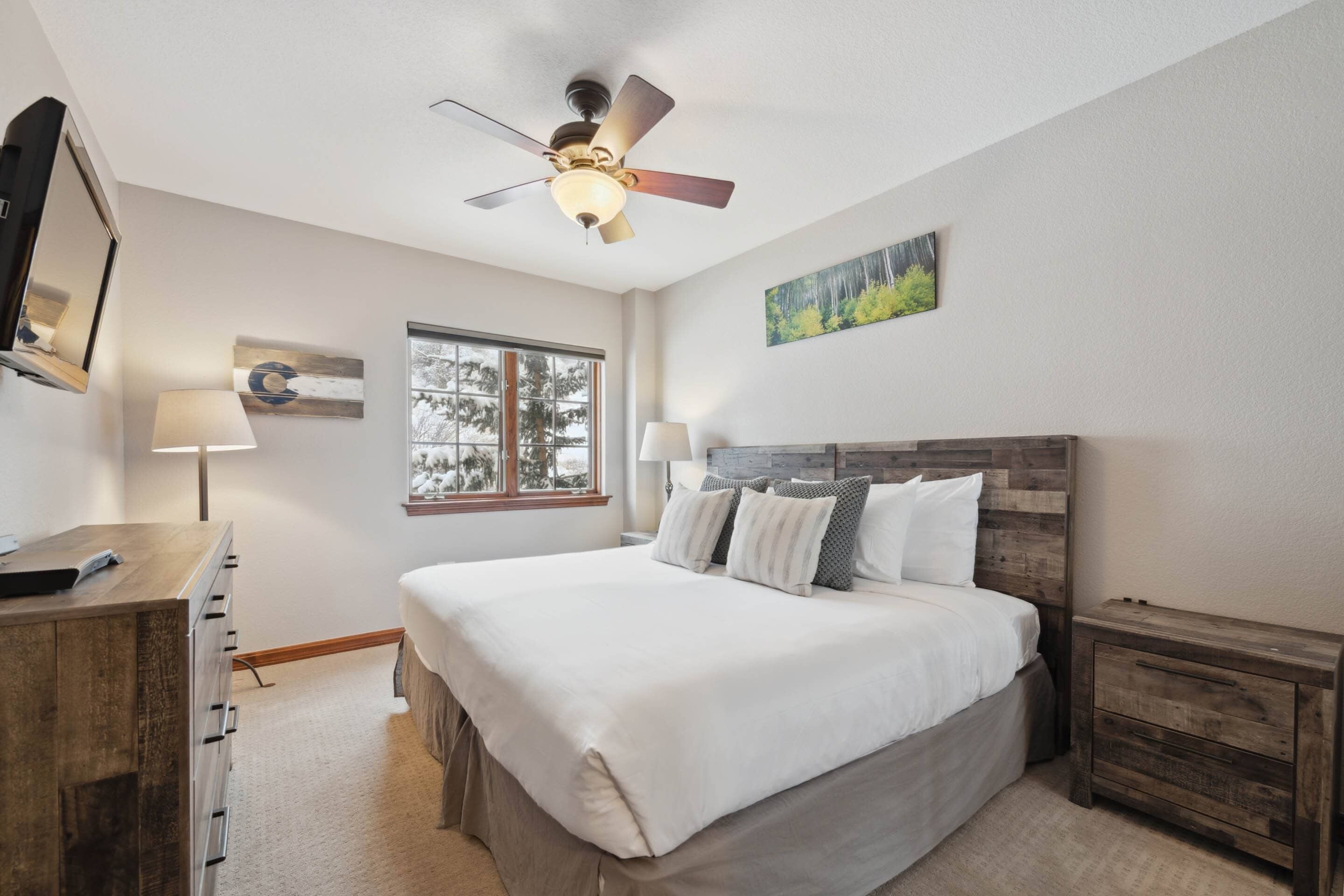 A bedroom with a bed, a ceiling fan, a window, a dresser, and a nightstand.