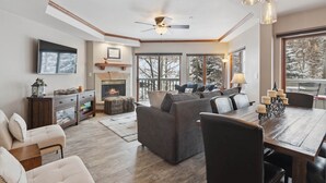 A spacious living room with a fireplace, large windows, and a dining area.
