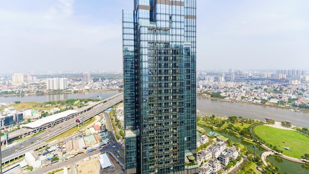 A high-rise building with a glass facade, surrounded by a cityscape and a river. - Luxury Landmark - Linh's Apartment (Ho Chi Minh City)