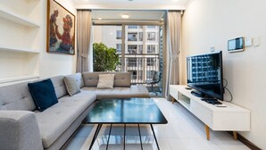 A modern living room with a grey sofa, a glass coffee table, a flat-screen TV, and a large window offering a view of a building. - Luxury Landmark - Linh's Apartment (Ho Chi Minh City)