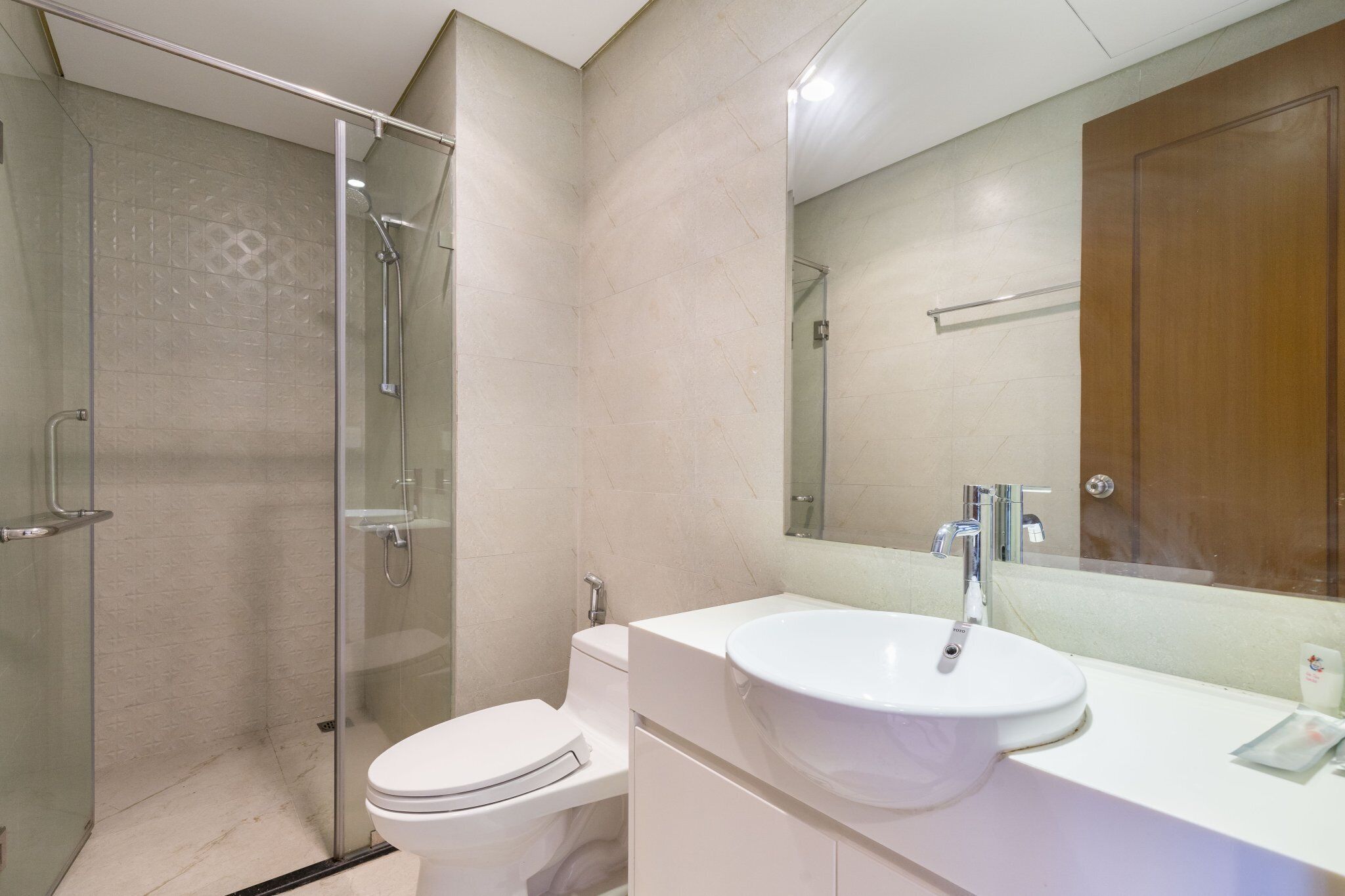 A modern bathroom with a glass-enclosed shower, a white toilet, and a large sink with a mirror above it.