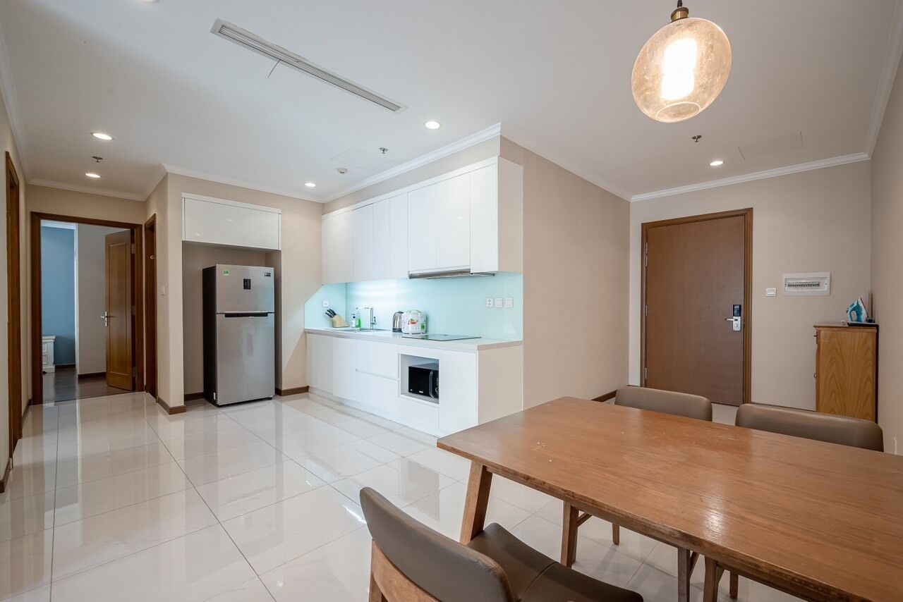 A modern kitchen with white cabinets, a built-in oven, and a dining area with a wooden table and chairs.