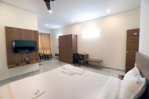 A hotel room with a bed, a desk, a chair, a TV mounted on the wall, and a wardrobe. - KCG Residency (Mysore)