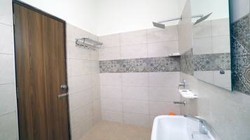 A small bathroom with a wooden door, a shower, a sink, and a mirror.