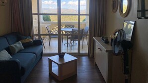 Una sala de estar con sofá, una mesa de centro, una mesa de comedor con sillas y un balcón con vistas al campo.