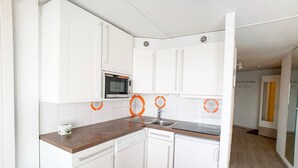 A compact kitchen with white cabinets, a built-in oven, a sink, and a dishwasher.