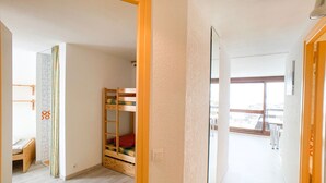 A room with a bunk bed, a small desk, and a window with a view of buildings.