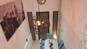 Un comedor con una mesa redonda, sillas azules, una lámpara colgante y un reloj en la pared.
