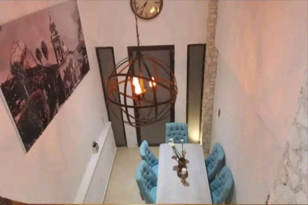 A dining area with a round table, blue chairs, a hanging light fixture, and a clock on the wall.
