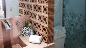 Un baño con pared de azulejos, un lavamanos, un inodoro y una zona de ducha.