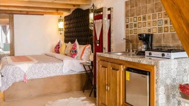 Un dormitorio con cama, una kitchenette pequeña con cafetera y un salpicadero de azulejos.