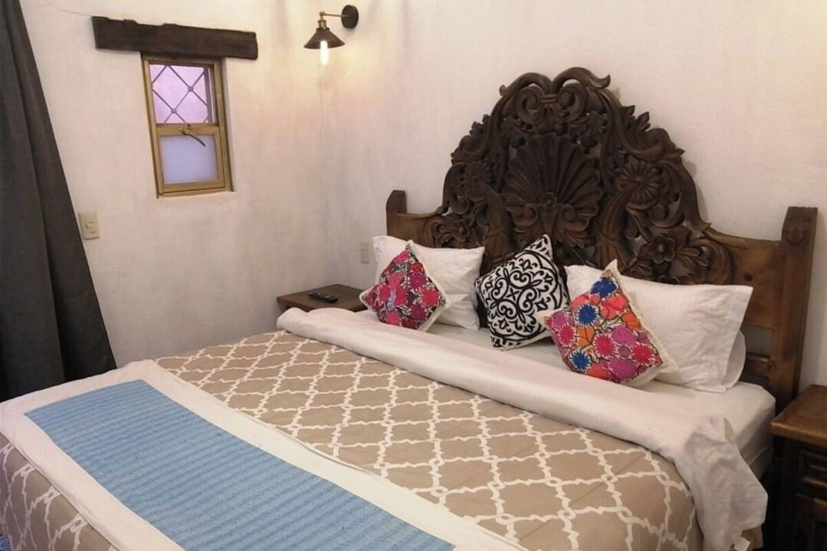 A bed with a patterned bedspread, a decorative headboard, and several pillows with various designs.