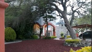 Un jardín ajardinado con un sendero de grava roja, un muro de piedra y un edificio con un arcojón rojo.