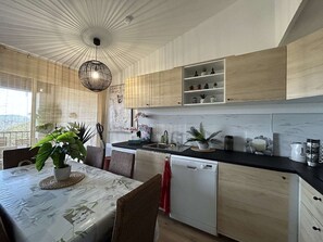 A modern kitchen with wooden cabinets, a dishwasher, and a dining area with a table and chairs. - Grimaud: 3-Room Apartment with Pool and Sea View (Grimaud)