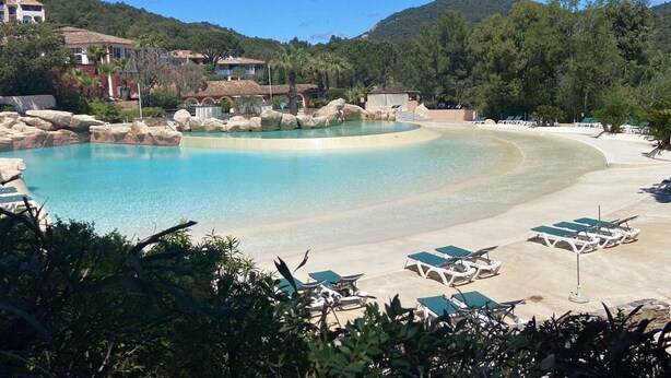 A resort with a large pool, lounge chairs, and a mountainous backdrop.
