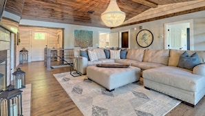 A spacious living room with a large sectional sofa, a wooden ceiling, and a chandelier.