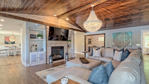 A spacious living room with a large sectional sofa, a fireplace, and a wooden ceiling.
