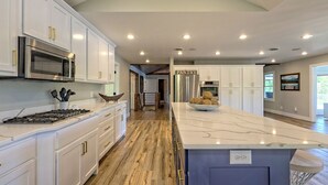 A modern kitchen with white cabinetry, stainless steel appliances, a marble island, and a wooden floor.
